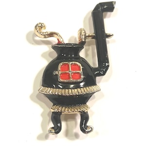 May include: Black and gold enamel stovetop brooch with a red window and a black pipe.