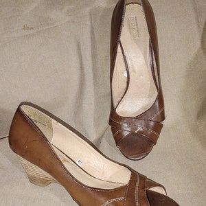 May include: Brown leather wedge sandals with open toes. The sandals have a crisscross design across the top and a wooden wedge heel. The brand name "MERONA" is visible inside one shoe. Size 9.5.