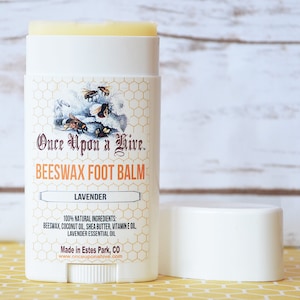 May include: A white tube of lavender beeswax foot balm with a label that reads "Once Upon a Hive. Beeswax Foot Balm Lavender 100% Natural Ingredients: Beeswax, Coconut Oil, Shea Butter, Vitamin E Oil, Lavender Essential Oil Made in Estes Park, CO www.onceupon ahive.com"