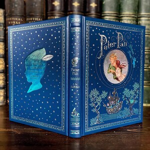 May include: A hardcover book titled "Peter Pan" by J.M. Barrie. The book has a blue cover with silver foil accents, including stars and illustrations of Peter Pan and other characters. The spine features the title and author.