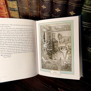 May include: An open book with a detailed illustration of a bedroom scene, framed in a light blue border. The illustration is in black and white, depicting a bed, open window, and figures. The book is surrounded by other antique books.