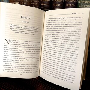 May include: An open book with text on aged paper. The pages display text from a classic work, with chapter headings and page numbers visible. The book is likely a historical or literary text, with a focus on the written word.