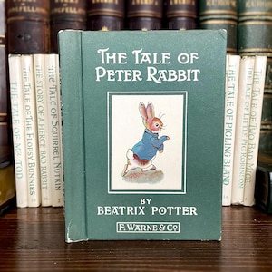 May include: A vintage copy of "The Tale of Peter Rabbit" by Beatrix Potter. The book has a green cover with the title in white and an illustration of Peter Rabbit. Other books are visible in the background.