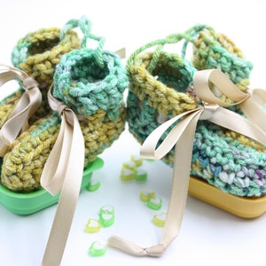 May include: A pair of green and yellow crocheted baby booties with beige satin ribbon ties. The booties are sitting on a green and yellow tray.