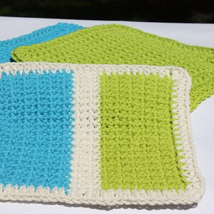 May include: Three crocheted dishcloths, one with a blue and white striped pattern, one with a green and white striped pattern, and one solid green. All dishcloths have a white crocheted border.
