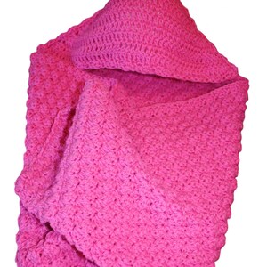 May include: A bright pink, handmade crochet baby blanket with a hood. The blanket is folded, showcasing the textured stitch pattern. The hood is visible at the top, and the blanket is made of soft yarn.