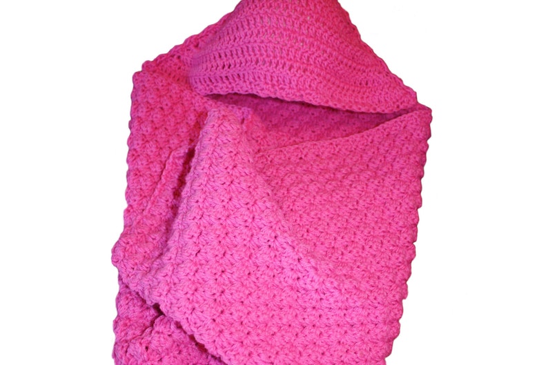 May include: A bright pink, handmade crochet baby blanket with a hood. The blanket is folded, showcasing the textured stitch pattern. The hood is visible at the top, and the blanket is made of soft yarn.
