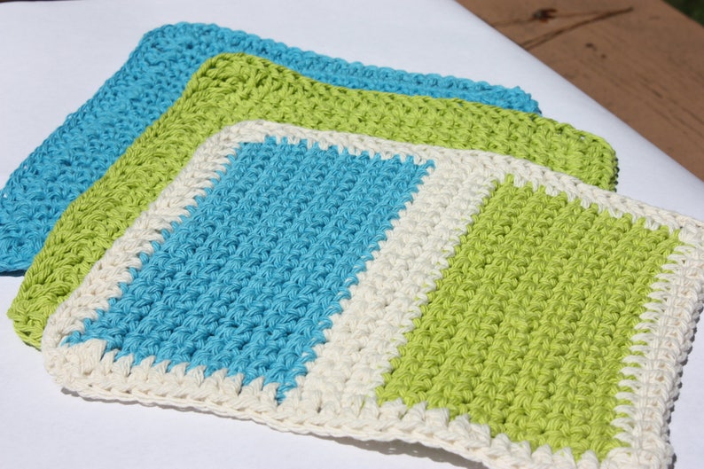 May include: Three crocheted dishcloths in blue, green, and white. The dishcloths are made with a simple stitch and have a square shape.
