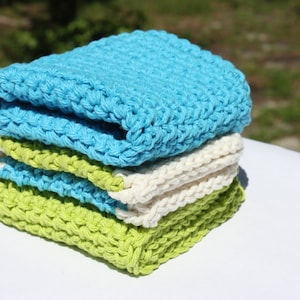 May include: A stack of four crocheted dishcloths in blue, white, and green. The dishcloths are made of cotton yarn and are perfect for cleaning dishes or wiping down surfaces.