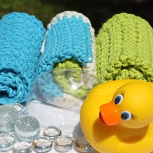 May include: Three crocheted washcloths in blue, white, and green, rolled up and displayed with a yellow rubber duck and clear glass beads.