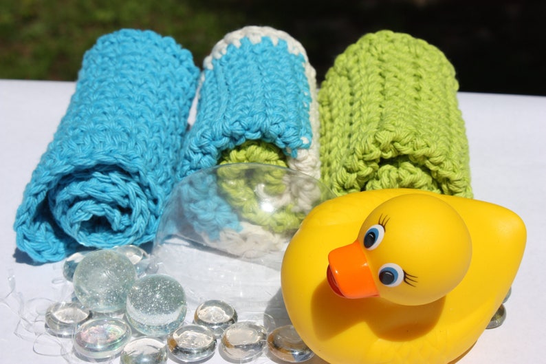 May include: Three crocheted washcloths in blue, white, and green, rolled up and displayed with a yellow rubber duck and clear glass beads.