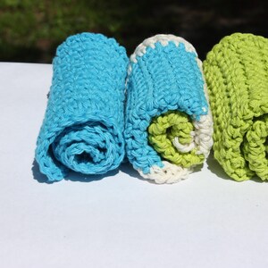 May include: Three rolled up crocheted dishcloths in blue, white, and green.