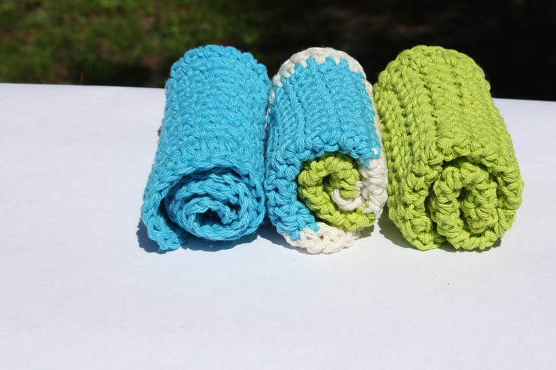 May include: Three rolled up crocheted dishcloths in blue, white, and green.
