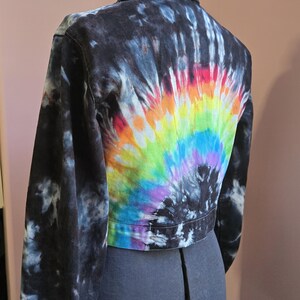 May include: Black denim jacket with a vibrant tie-dye design. The back of the jacket features a rainbow of colors, including red, orange, yellow, green, blue, and purple. The sleeves and shoulders have a black and white pattern.