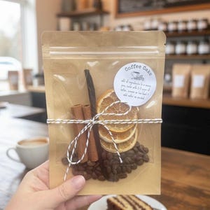 May include: A clear bag filled with coffee beans, cinnamon sticks, dried orange slices, and a vanilla bean, tied with twine. A sticker reads "Coffee Oake". A slice of coffee cake sits on a white plate.