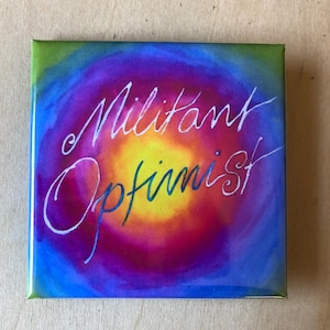 Könnte beinhalten: Quadratischer Knopf mit einem lebendigen, farbenfrohen Design. Das Kunstwerk zeigt ein wirbelndes Muster aus Blau-, Lila-, Grün- und Gelbtönen. Die Worte "Militant Optimist" sind in einer fließenden, weißen Schrift über die Mitte des Knopfes geschrieben.