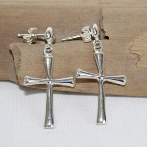 May include: A pair of silver cross earrings. The earrings are dangle style with a simple cross design.
