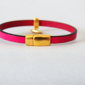 Op de afbeelding: Een roze leren armband met een gouden magneetsluiting.