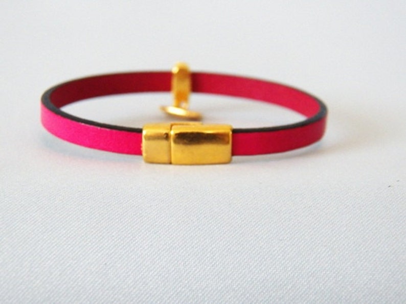Op de afbeelding: Een roze leren armband met een gouden magneetsluiting.