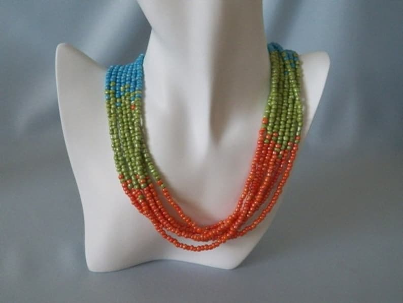 May include: A multi-strand necklace made of small beads in shades of blue, green, and orange. The necklace is layered and hangs in a cascading pattern.
