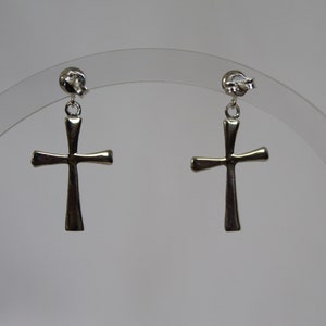May include: A pair of silver cross dangle earrings. The earrings are on a clear display stand.