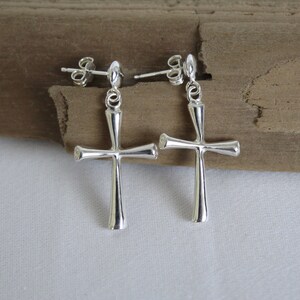 May include: A pair of silver cross earrings with a simple design. The earrings are made of metal and have a post back.