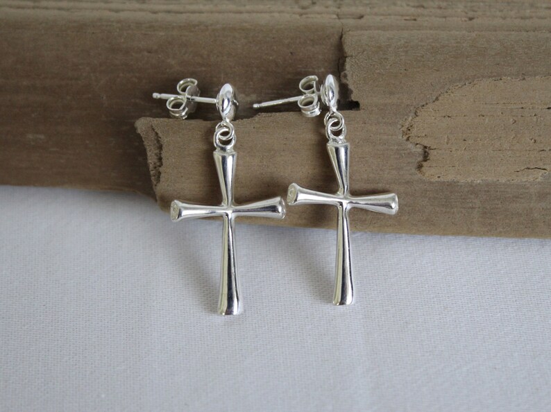 May include: A pair of silver cross earrings with a simple design. The earrings are made of metal and have a post back.
