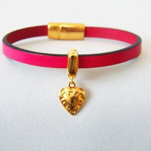 Op de afbeelding: Een roze leren armband met een gouden magneetsluiting en een gouden hartbedel.
