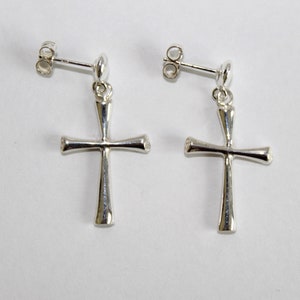 May include: A pair of silver dangle earrings with a simple cross design. The earrings have a post back closure.
