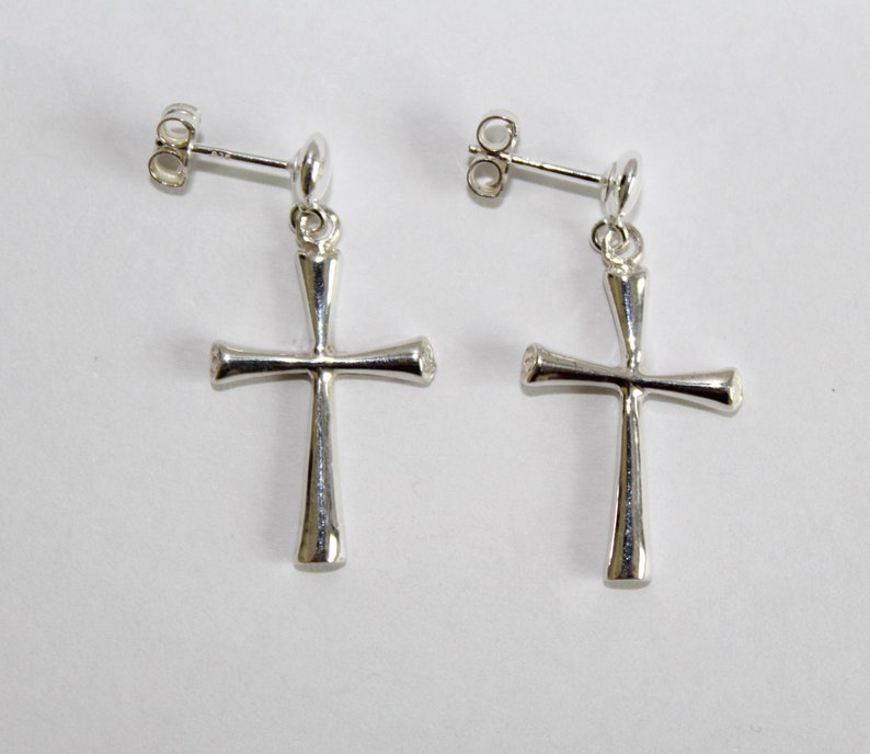 May include: A pair of silver dangle earrings with a simple cross design. The earrings have a post back closure.