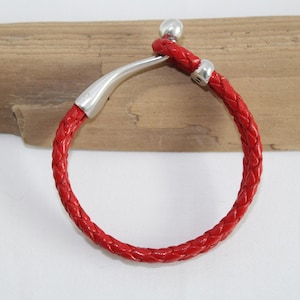 May include: A red braided leather bracelet with silver metal accents. The bracelet has a simple design and is adjustable.