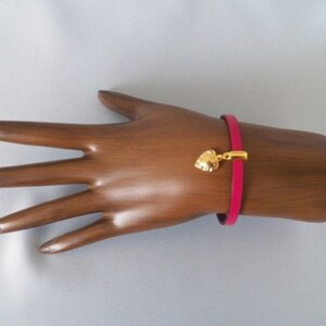 Op de afbeelding: Een roze leren armband met een gouden hartbedel.