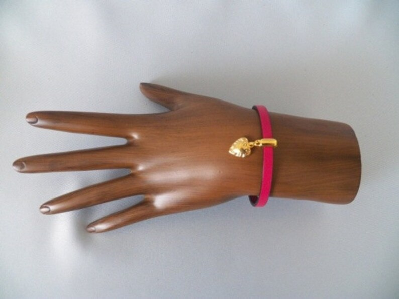 Op de afbeelding: Een roze leren armband met een gouden hartbedel.
