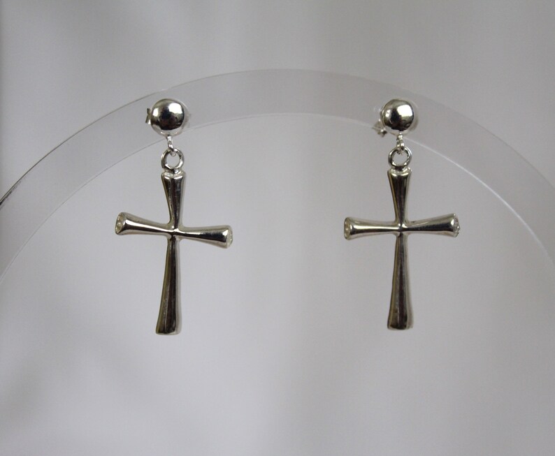 May include: A pair of silver cross earrings with a simple design. The earrings are hanging from a small ball.