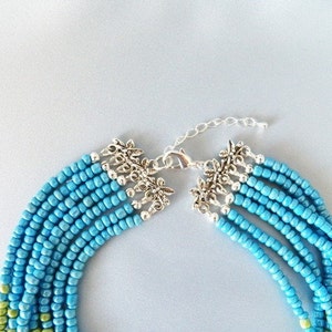 May include: A multi-strand necklace made of turquoise blue and green seed beads with a silver clasp and decorative floral accents.