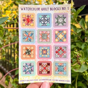 May include: A sheet of stickers featuring watercolor quilt block designs. Each square block showcases a unique geometric pattern in various colors, including red, blue, and orange, set against pastel backgrounds. The text "WATERCOLOR QUILT BLOCKS NO. 1" is at the top.