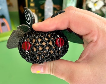 May include: A black chainmail ball with red bead eyes and black leather wings. The ball is held in a hand.
