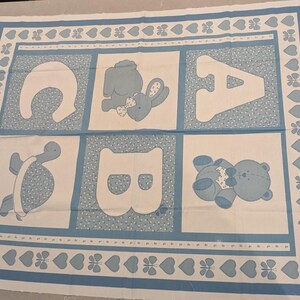 May include: A baby quilt panel featuring the letters A, B, and C, along with images of a turtle, a bunny, and a teddy bear. The design is in shades of blue and white, with a border of hearts and butterflies.