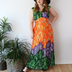 May include: A sleeveless maxi dress featuring a leaf pattern in green, orange, and purple. The dress is worn with a black hat. The dress has a fitted bodice and a flowing skirt, ideal for a summer day.