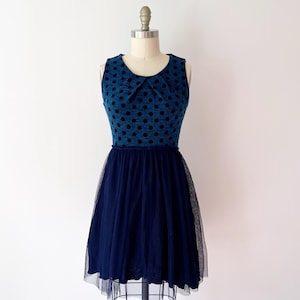 May include: A sleeveless blue dress with black polka dots on the bodice and a navy blue tulle skirt. The dress is displayed on a mannequin. The bodice has a small collar.