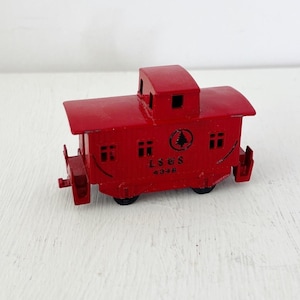 May include: A small, red toy caboose with black wheels. The caboose has a small cabin on top and windows on the sides. The text "LS&S 4348" and a tree logo are visible on the side.