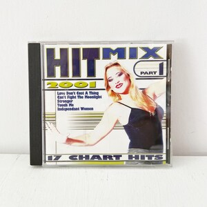 Puede incluir: Una caja de CD de Hitmix 2001 Part 1, con una mujer con un top negro. La portada incluye el texto "Hitmix 2001" y una lista de canciones, incluyendo "Love Don't Cost A Thing" y "17 Chart Hits."
