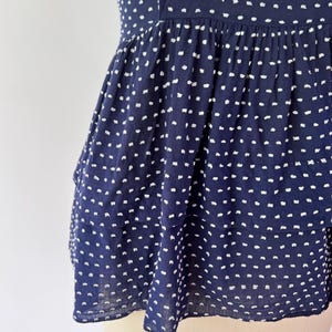 May include: Navy blue top with white polka dots. The top features a tiered, peplum-style design. The fabric appears lightweight and textured, with a subtle crinkled effect. The garment is displayed on a mannequin.