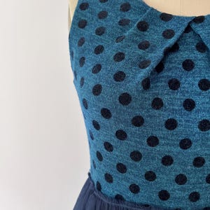 May include: A teal dress with black polka dots and a navy blue tulle skirt. The sleeveless dress has a Peter Pan collar. The fabric has a textured appearance, and the polka dots are evenly spaced across the bodice.