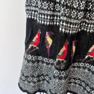 May include: A black and white patterned skirt with a bird design. The skirt features a geometric pattern in black and white, with a band of black fabric at the bottom with colorful bird illustrations.