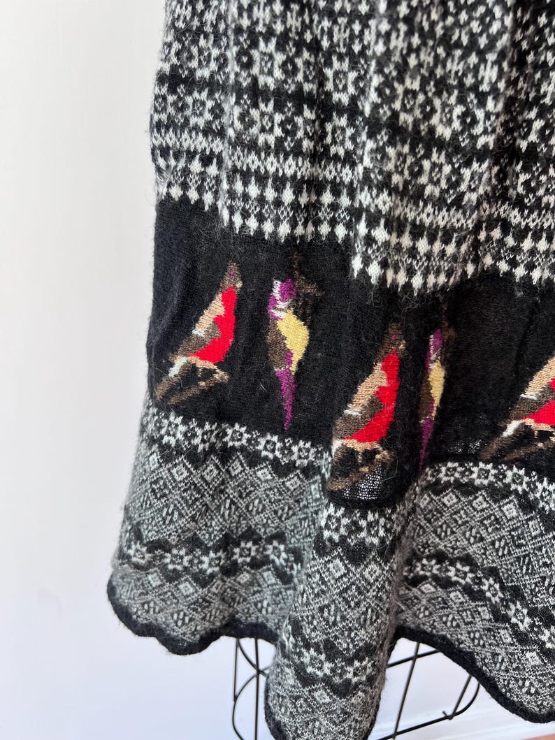 May include: A black and white patterned skirt with a bird design. The skirt features a geometric pattern in black and white, with a band of black fabric at the bottom with colorful bird illustrations.
