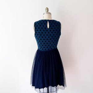 May include: A navy blue dress with a textured bodice and black polka dots. The dress has a keyhole back and a full, layered tulle skirt. The dress is displayed on a mannequin.