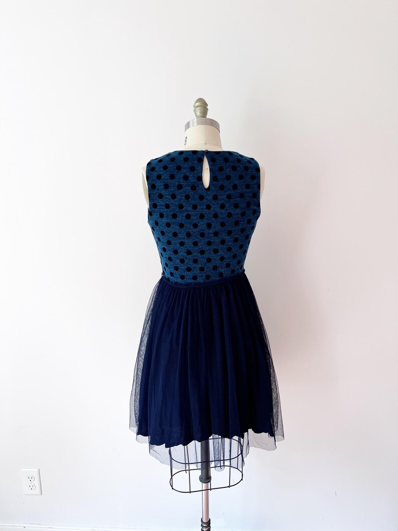 May include: A navy blue dress with a textured bodice and black polka dots. The dress has a keyhole back and a full, layered tulle skirt. The dress is displayed on a mannequin.