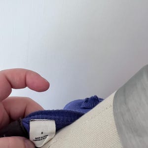 Op de afbeelding: Een close-up van een paars kledingstuk met een label met de tekst "S" en "MADE IN CHINA FABRIQUE EN CHINE". Het kledingstuk staat op een mannequin. Het label wordt door een hand vastgehouden.