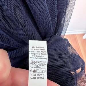 May include: Close-up of navy blue netting fabric. A white tag lists the fabric composition as 95% polyester, 5% polyurethane, 100% rayon flock, 95% rayon lining, 5% spandex, and 100% nylon netting. Care instructions are also listed.